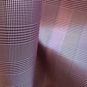 May include: A close-up of a pink and black plaid fabric. The fabric is folded in half, and the plaid pattern is visible on both sides.