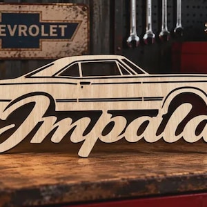 May include: A light-coloured wooden cutout featuring the side profile silhouette of a classic Chevrolet Impala car. The word Impala is written in a large, cursive script font integrated into the lower section of the vehicle's body design.