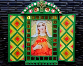 Könnte beinhalten: Ein grüner Holzrahmen mit einem farbenfrohen Mosaikdesign und einem kleinen Fenster mit einem religiösen Bild einer Frau, die eine rote Blume hält. Der Rahmen hat oben ein Kreuz.