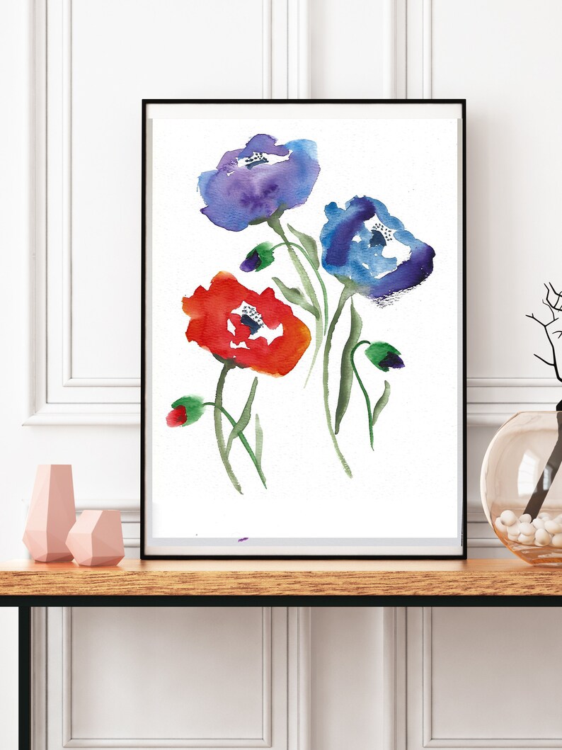 Puede incluir: Una pintura de acuarela enmarcada de tres flores. Las flores son azules, rojas y moradas. La pintura est&aacute; sobre un fondo blanco.