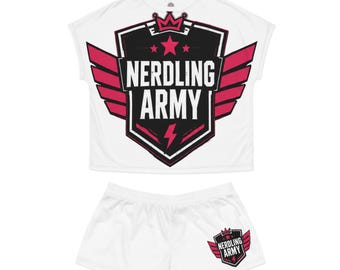 May include: A white short-sleeved top and matching shorts set. The top features a large black shield graphic with pink wings, a crown, stars, a lightning bolt, and the text NERDLING ARMY. The shorts feature a smaller version of the same graphic.
