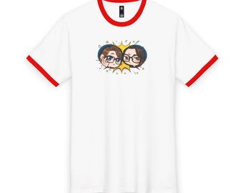 May include: A white ringer t-shirt with red trim on the collar and sleeve cuffs. The center of the chest features a graphic illustration of two chibi-style characters with glasses, framed by a yellow starburst shape and small gold stars.
