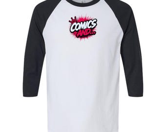 May include: A white baseball t-shirt with black three-quarter length sleeves. The center of the chest features a graphic with a pink paint splatter effect, a small red crown icon, and the bold black and white text that reads COMICS AND...