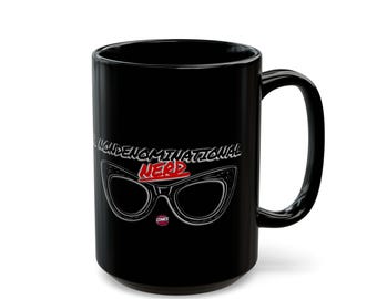 May include: A black ceramic mug featuring a graphic of black cat-eye glasses. Above the glasses, the text reads "NON-DENOMINATIONAL" in white, and below, the word "NERD" is printed in bold red letters. A small circular logo is visible below the glasses.