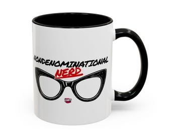 May include: A white ceramic mug with a black handle and interior rim. The front features the black text NONDENOMINATIONAL, the red text NERD, and a graphic of black cat-eye glasses. A small red and white logo is positioned below the glasses.