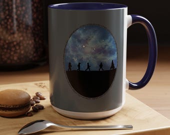 May include: A ceramic mug with a dark blue interior and handle. The exterior is gray with a circular design featuring silhouettes of figures walking against a starry night sky. A decorative item for the kitchen.