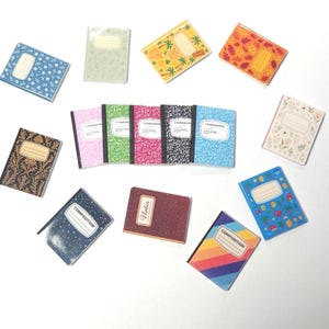 May include: A collection of miniature composition notebooks in various colors and patterns. The notebooks feature designs such as floral, geometric, and striped patterns. Some notebooks have the word "Notes" or "Composition" on the cover. The notebooks are arranged on a white surface.