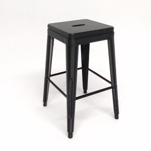 May include: A black metal stool with a square seat and four legs. The stool has a minimalist design with a footrest and a small slot cut into the seat. The stool is made of metal and has a matte finish.
