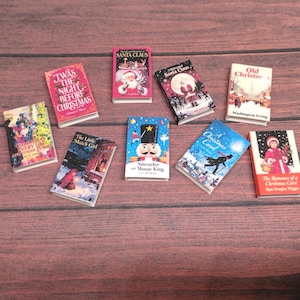 May include: A collection of miniature Christmas-themed books with colorful covers. Titles include "Twas the Night Before Christmas," "Santa Claus," and "A Christmas Carol." The books are arranged on a wooden surface.