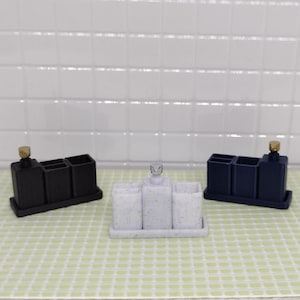 May include: Three bathroom countertop organizers, one black, one white with black speckles, and one blue. Each organizer has a dispenser and multiple compartments.