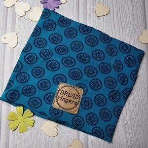 May include: A teal blue fabric headband with a dark blue circular pattern. The headband has a brown leather patch with the text "Dread ringers" stitched in brown thread.