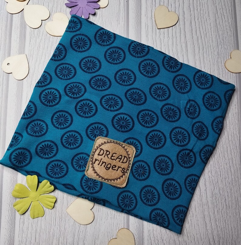 May include: A teal blue fabric headband with a dark blue circular pattern. The headband has a brown leather patch with the text "Dread ringers" stitched in brown thread.