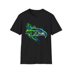 Op de afbeelding: Een zwart t-shirt met korte mouwen en een grafische print van een gestileerde adelaarskop in profiel. Het ontwerp bevat het silhouet van een stadsskyline in neon-groene en blauwe tinten met abstracte verfspatten rondom de vogel.