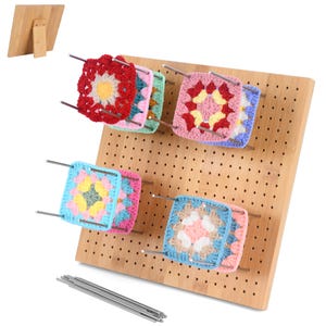 May include: A wooden pegboard with colorful, square crochet pieces attached with metal rods. The crochet squares feature various colors and patterns, including red, pink, blue, and yellow. A wooden stand is visible in the background, and a set of metal rods are in the foreground.