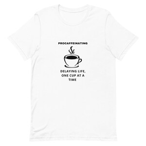 May include: White t-shirt with a black graphic of a steaming coffee cup. The text above the cup reads "PROCAFFEINATING", and below it says "DELAYING LIFE, ONE CUP AT A TIME".