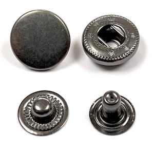 May include: Four black metal snap fasteners. Two are round with a decorative edge and a hole in the center. The other two are round with a raised center.