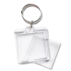 May include: A clear plastic photo frame keychain with a silver key ring. The frame is square and has a smaller, clear plastic insert that can be used to hold a photo or other small item.