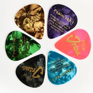 May include: Six guitar picks with different colors and designs. Each pick has the word "Jesus" and the phrase "Psalm 149:1" printed on it. The picks are arranged in a circle.