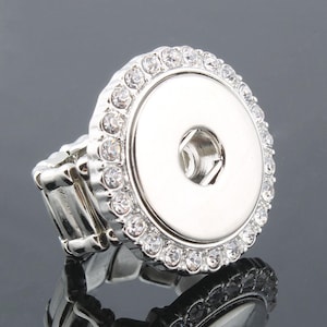 May include: A silver ring with a large, round, rhinestone-encrusted button. The button has a silver center with a small hole in the middle.