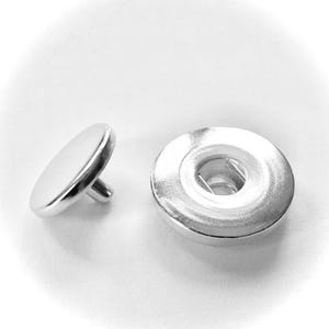 May include: Two silver metal snap fasteners, one with a flat top and the other with a round top and a center hole.