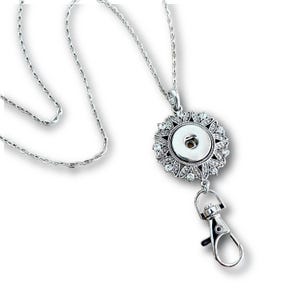 May include: Silver chain with a silver flower-shaped charm with rhinestones and a snap button in the center. The chain has a silver lobster clasp.