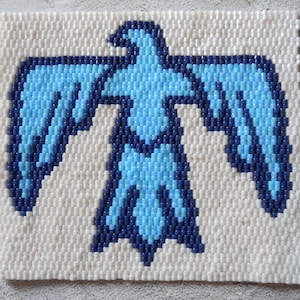 May include: A blue and white beaded bird design on a white background. The bird is facing forward with its wings spread out.
