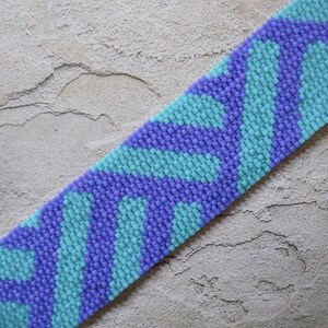 May include: A beaded bracelet with a wavy pattern in shades of purple and turquoise.