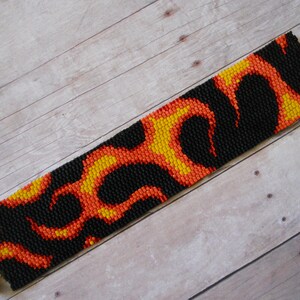 May include: A black, orange, and yellow beaded bracelet with a flame pattern. The bracelet has gold metal clasps.