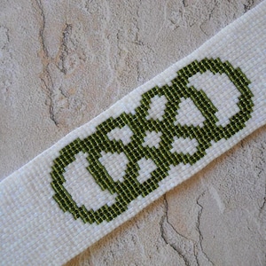May include: A white beaded bracelet with a green beaded design of three interlocking circles.