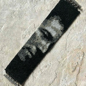 May include: A black beaded bracelet featuring a grayscale portrait design. The bracelet has a rectangular shape with a magnetic clasp. The portrait appears to be of a person's face, with details created using varying shades of gray and white beads.