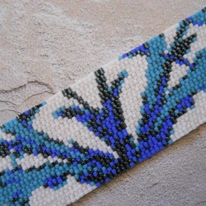 May include: A white beaded bracelet with a blue and black geometric pattern.