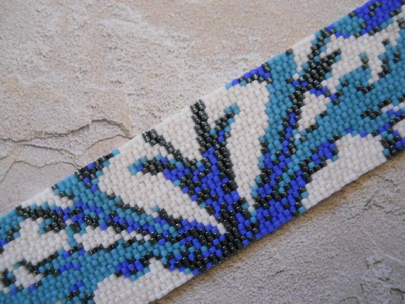 May include: A white beaded bracelet with a blue and black geometric pattern.