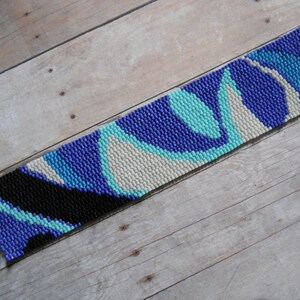 May include: A beaded bracelet with a blue, turquoise, white, and black geometric pattern. The bracelet has silver metal clasps.