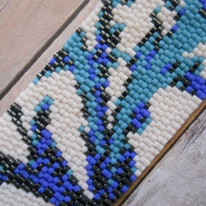 May include: A close-up of a beaded bracelet with a white background and a pattern of blue, black, and white beads.