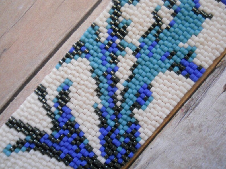 May include: A close-up of a beaded bracelet with a white background and a pattern of blue, black, and white beads.