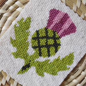 Puede incluir: Primer plano de una flor de cardo con cuentas, con hojas verdes y un centro rosa. El cardo está hecho con cuentas sobre un fondo blanco.