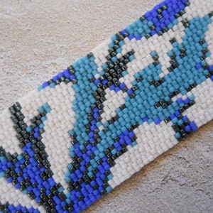 May include: A close-up of a beaded bracelet with a white background and a pattern of blue, black, and gray beads.