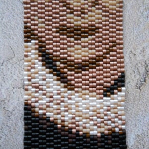 May include: A beaded bracelet with a pattern of brown, black, white, and pink beads. The beads are arranged in a geometric pattern.