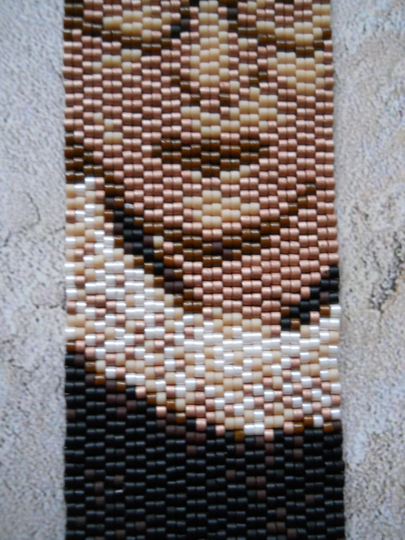 May include: A beaded bracelet with a pattern of brown, black, white, and pink beads. The beads are arranged in a geometric pattern.