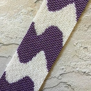 May include: A purple and white beaded bracelet with a wavy pattern. The bracelet is made of small, square beads.