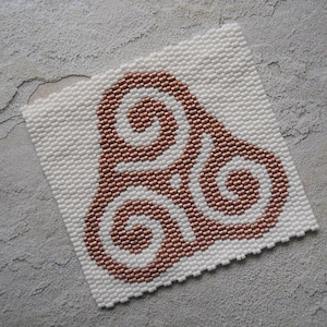 May include: A white square beaded coaster with a copper-colored Celtic knot design.