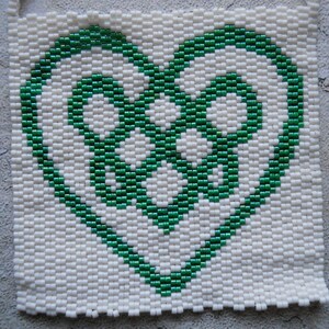 May include: A green heart-shaped design made of small beads on a white background.