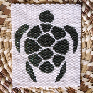 May include: A black and white beaded turtle design on a white background. The turtle is made of small black beads and is surrounded by white beads.