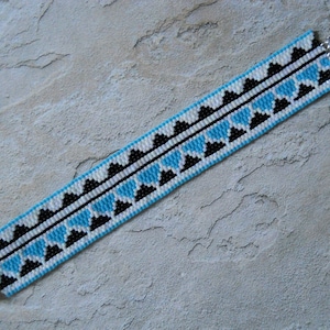 May include: A beaded bracelet with a geometric pattern in black, white, and blue. The bracelet has silver clasps on each end.