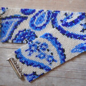 May include: A white beaded bracelet with a blue and black geometric pattern. The bracelet has silver toggle clasps.