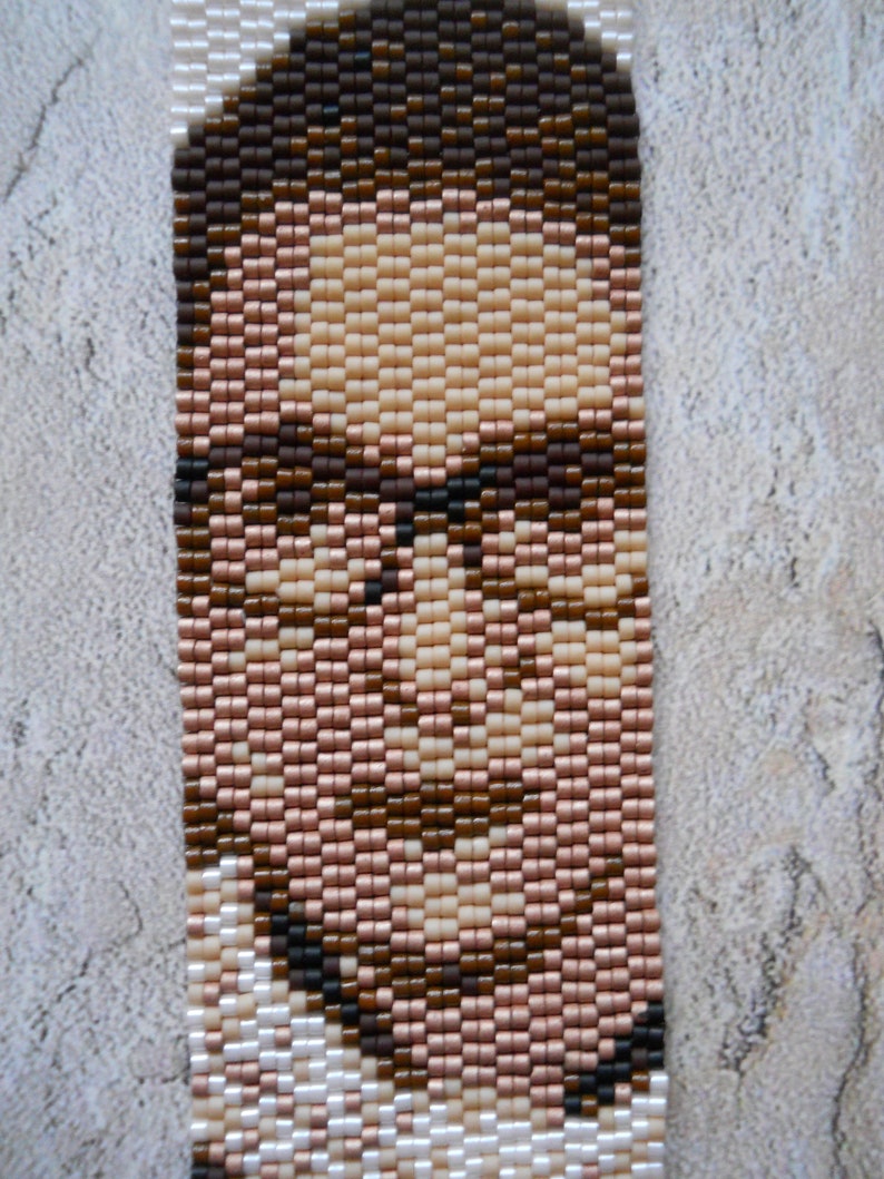 May include: A beaded portrait of a person with brown hair and glasses. The portrait is made with small, colorful beads.