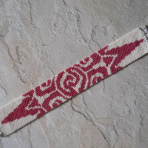 May include: A white and pink beaded bracelet with a geometric pattern. The bracelet has silver clasps.