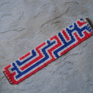 Könnte beinhalten: Ein rot-weiß-blaues Perlenarmband mit geometrischem Muster. Das Armband hat silberne Metallverschlüsse.