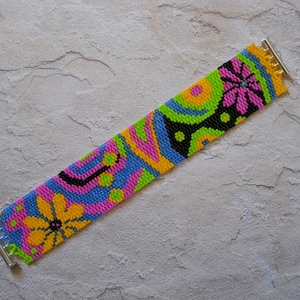 May include: A colorful beaded bracelet with a geometric and floral pattern in shades of pink, blue, green, yellow, and black.