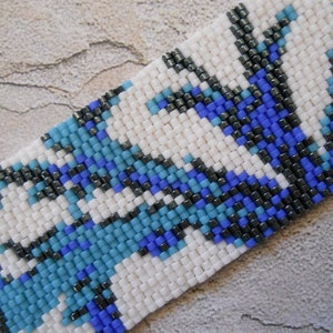 May include: A close-up of a beaded bracelet with a geometric pattern in white, blue, and black.